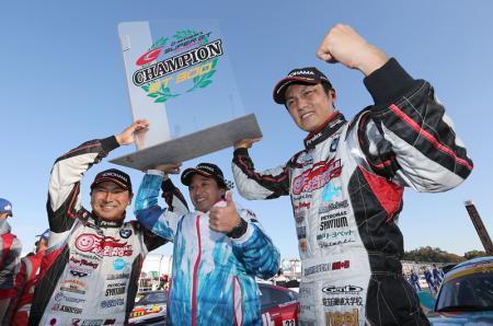 Drivers Nobuteru Taniguchi (right) and Tatsuya Kataoka (left) raise their GT300 championship trophy with team manager Ukyo Katayama 